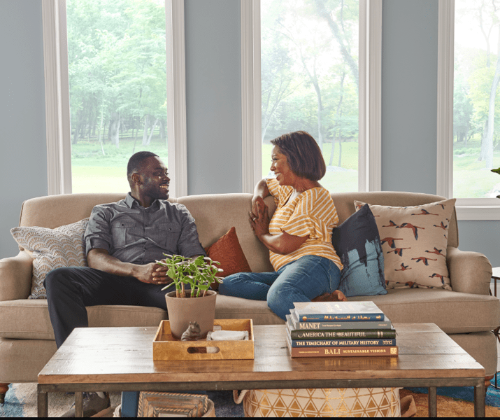 A man and woman sitting on a couch talking about their new 33NM3 domestic hot water air-to-water heat pump